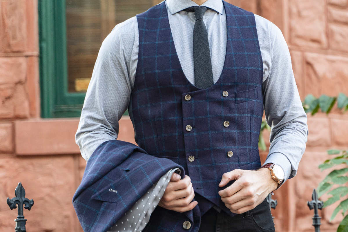 Man wearing shirt, tie and vest, holding his jacket