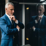 Mature businessman staring at himself in the glass-door and smiling pensively